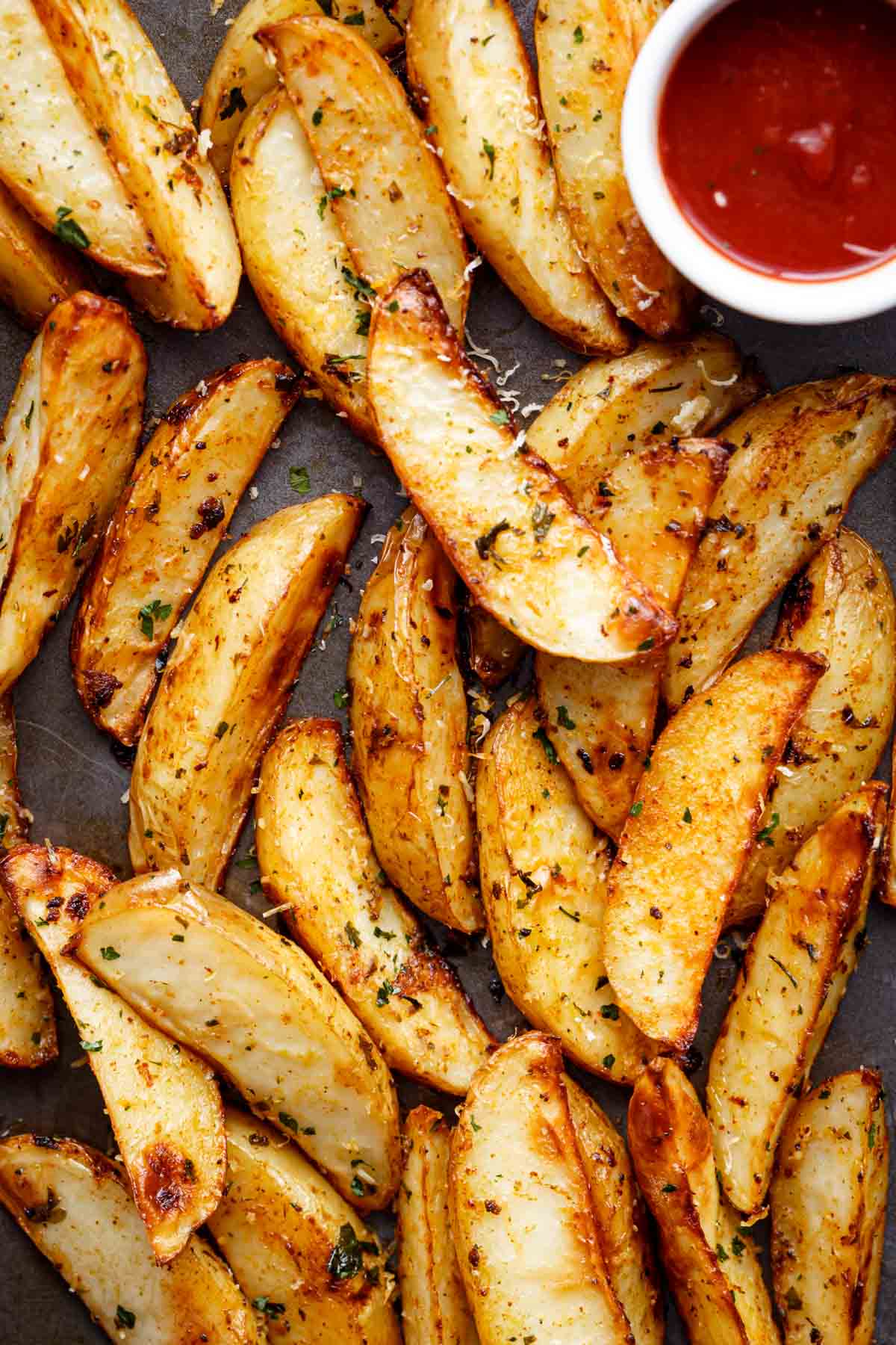 A top-view shot of baked potato wedges accompanied by a side of ketchup.