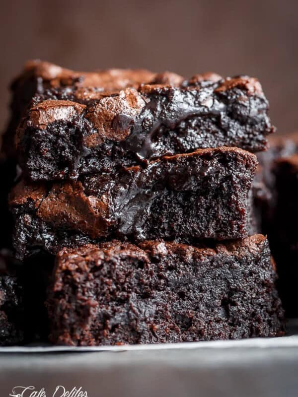 Side view of three slices of chocolate brownie stacked on top of each other. The brownies have a light brown top and dark, gooey interior.