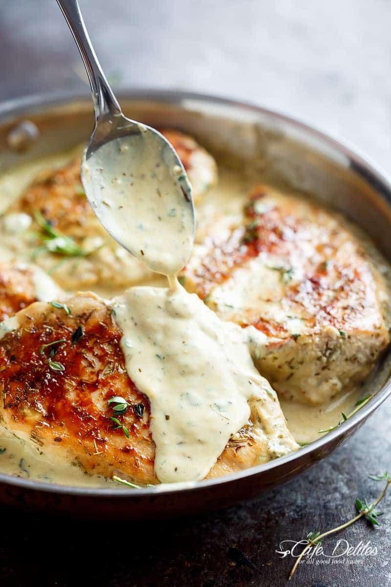 Close-up image of creamy chicken with herbs in a pan, being covered with its own sauce.