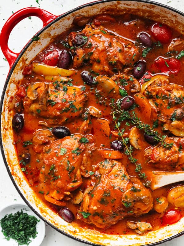 Spicy Five chicken pieces in a le creuset style casserole dish covered in red Chicken Cacciatore sauce. Olives, carrots and other vegetables are submerged in the sauce.
